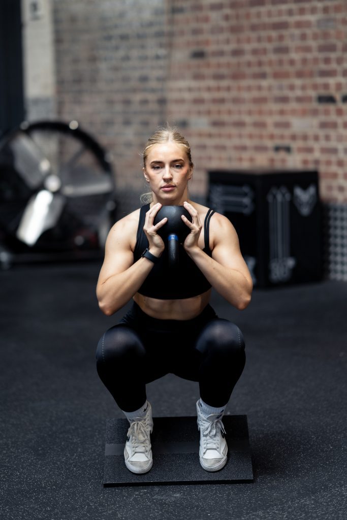 Woman performing a squat on the black wooden Forte Fitness slant board