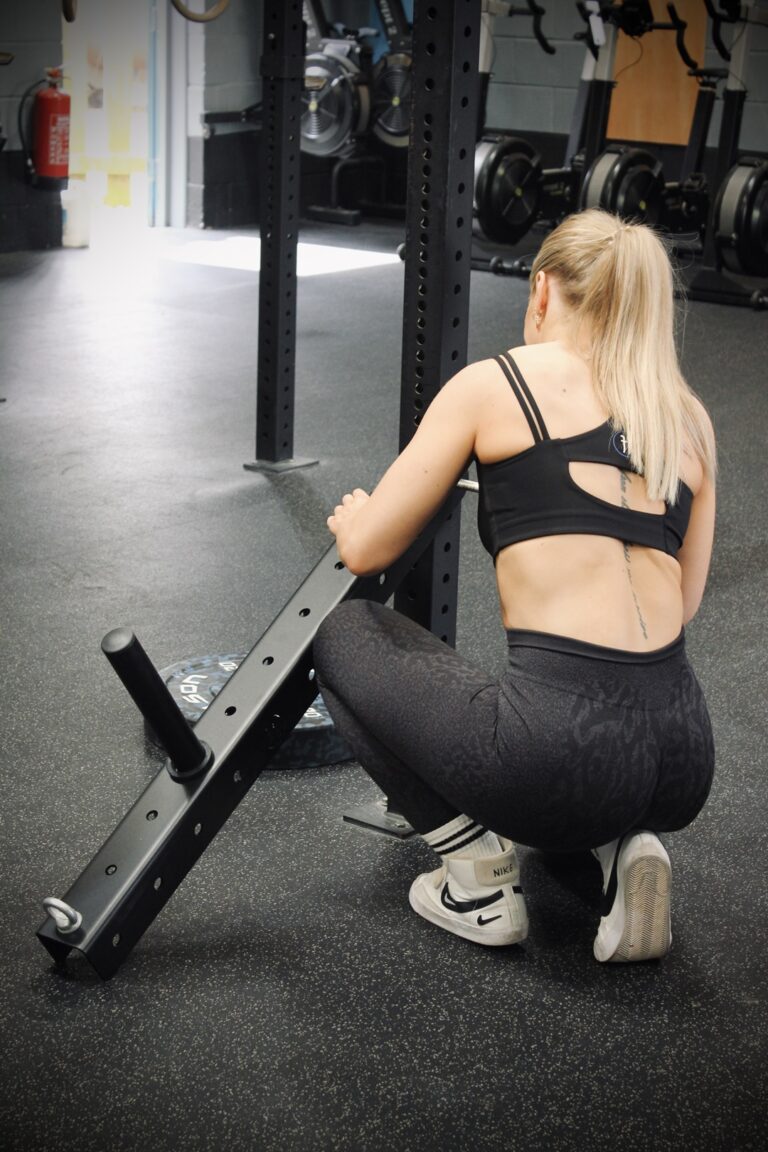 woman setting up a belt squat attachment on a rig