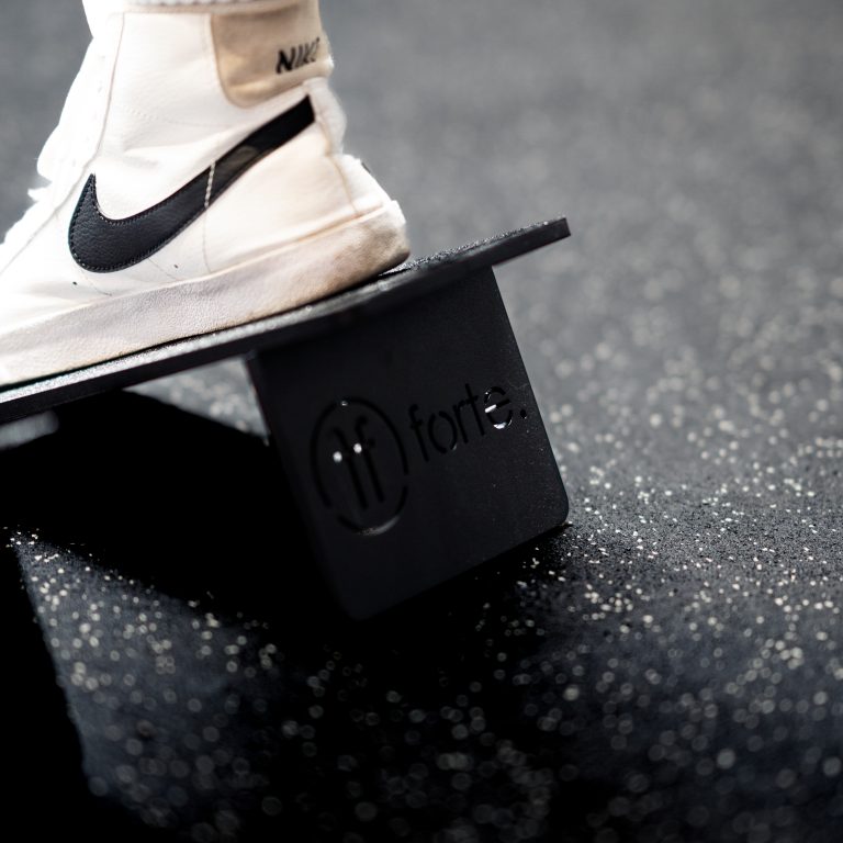 Foot wearing a Nike white shoe, on a Forte Fitness aluminium slant block