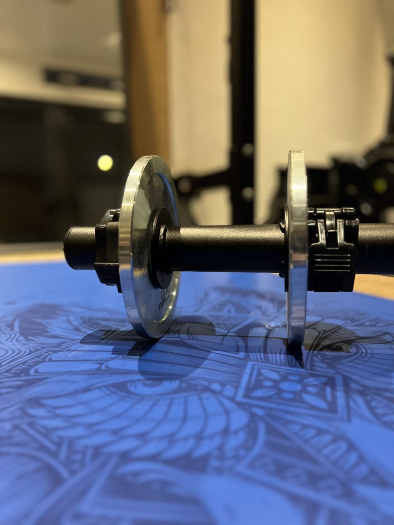 A Forte Fitness Axle Dumbbell with plates attached placed on a blue foor.