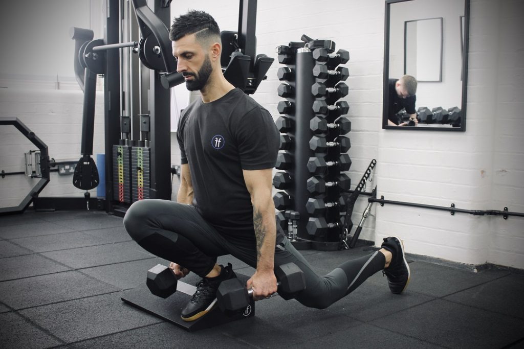 A man using the Forte Fitness incline boards. The man is holding weights in both his hands, with his foot placed at the bottom of the slant board to complete his lunge.