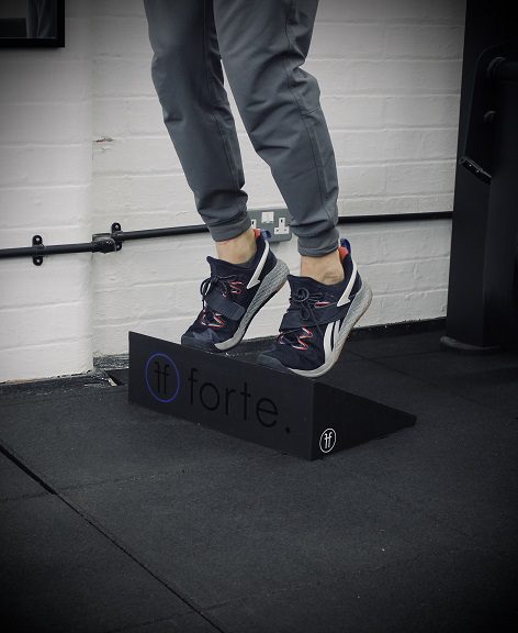 A slant board being used by a male. The male is on the tip of his toes at the top of the incline board.