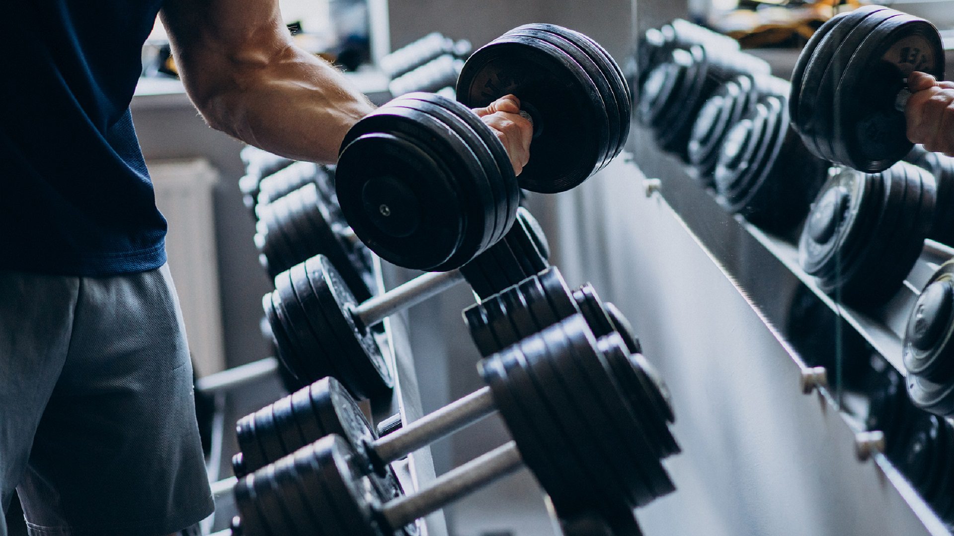 Man in a gym picking up an adjustable weight dumbbell ready to train