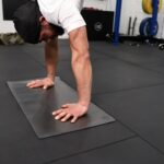 man performing a handstand in a gym using a handstand mat