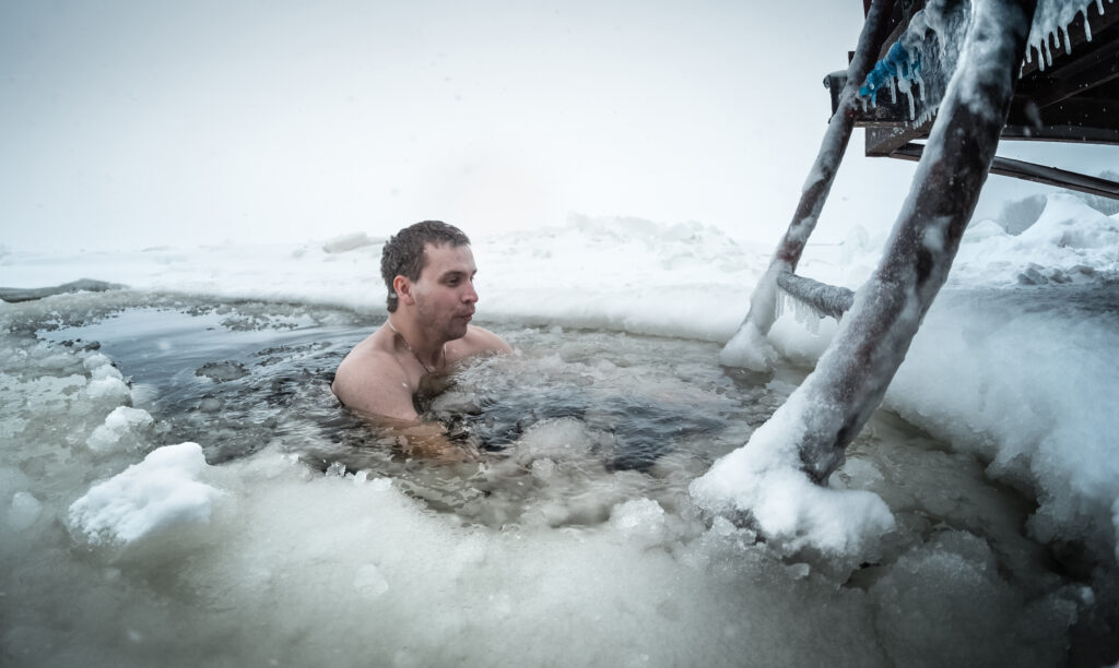 Young man swimming in the ice hole on a winter lake