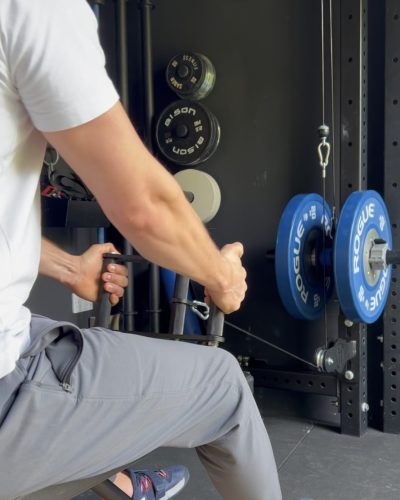 A man using a cable row attachment. The picture is taken facing towards the cable machine, and the back of the man, meaning that we can see the cable attachment being used.